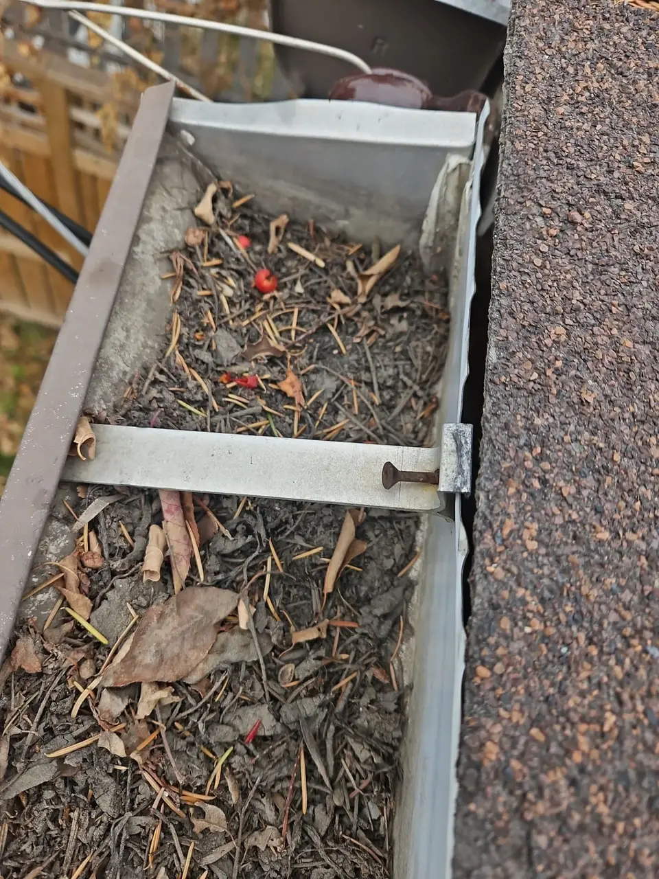 clogged eaves filled with leaves, asphalt granules and dirt piled through years on a Calgary bungalow