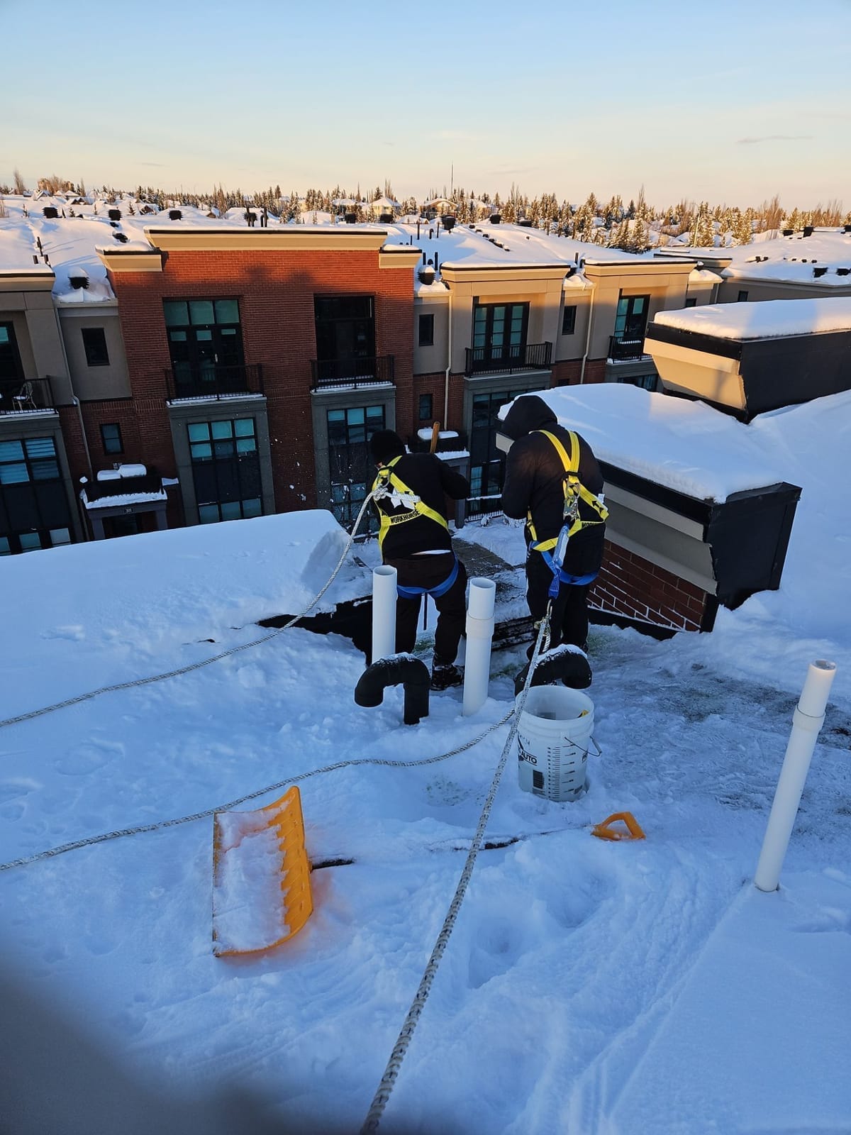 Harnessed CPR Group Roofers removing ice damming on a residential building in Calgary