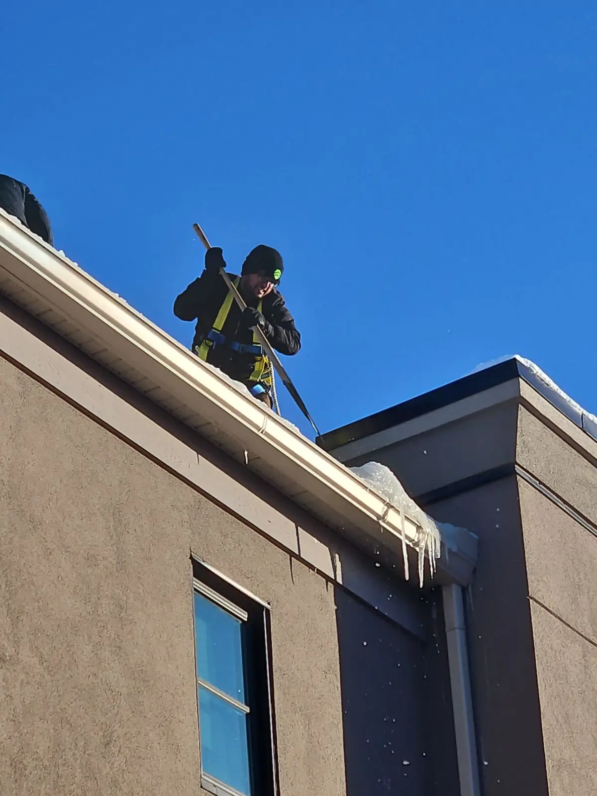 CPR Group roofer harnessed for snow removal on a low pitch roof in Calgary