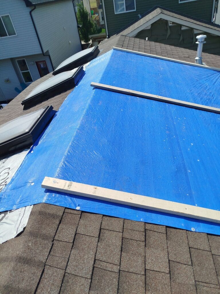 blue tarp acting as temporary fix to a damaged roof, re-enforced with three 2x6